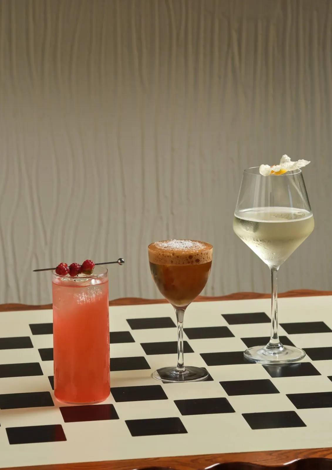 Three cocktails lined up on a black and white checkerboard table